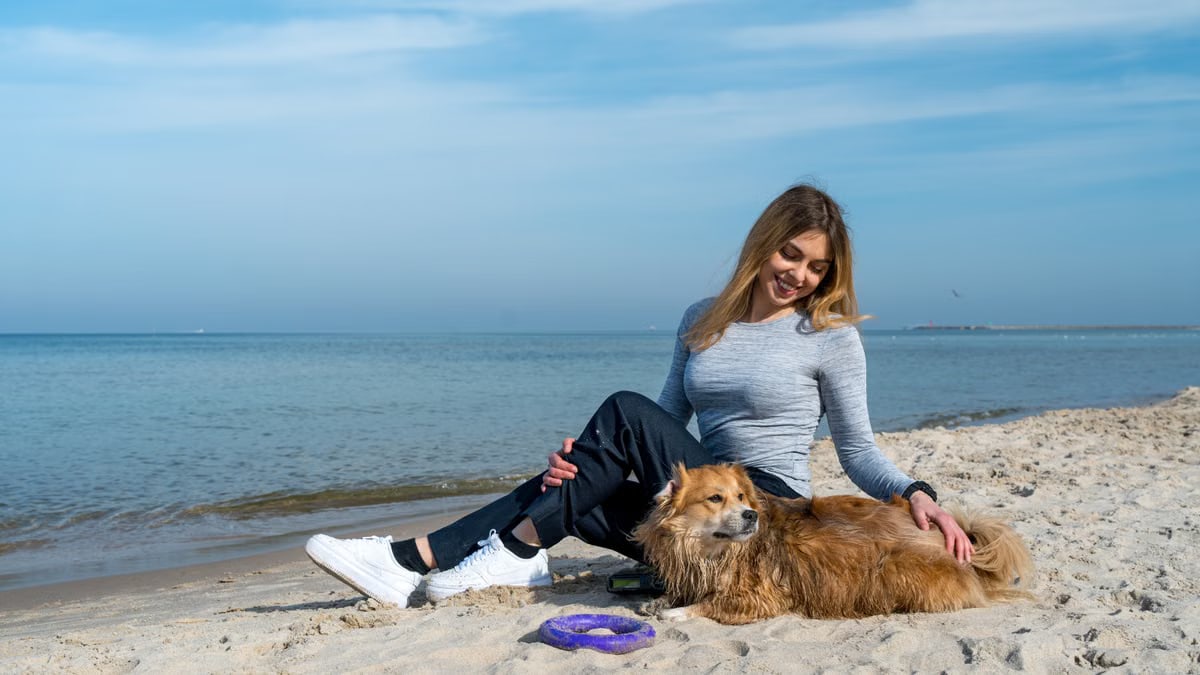 Woman enjoying a sunny day at Kołobrzeg beach with her dog, capturing a perfect seaside moment.